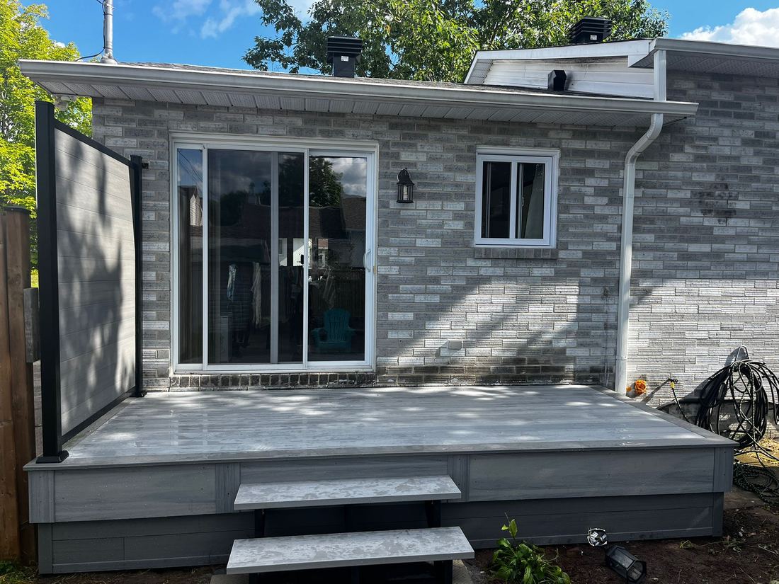 Grey composite deck with two steps and a black-framed privacy screen at a patio door