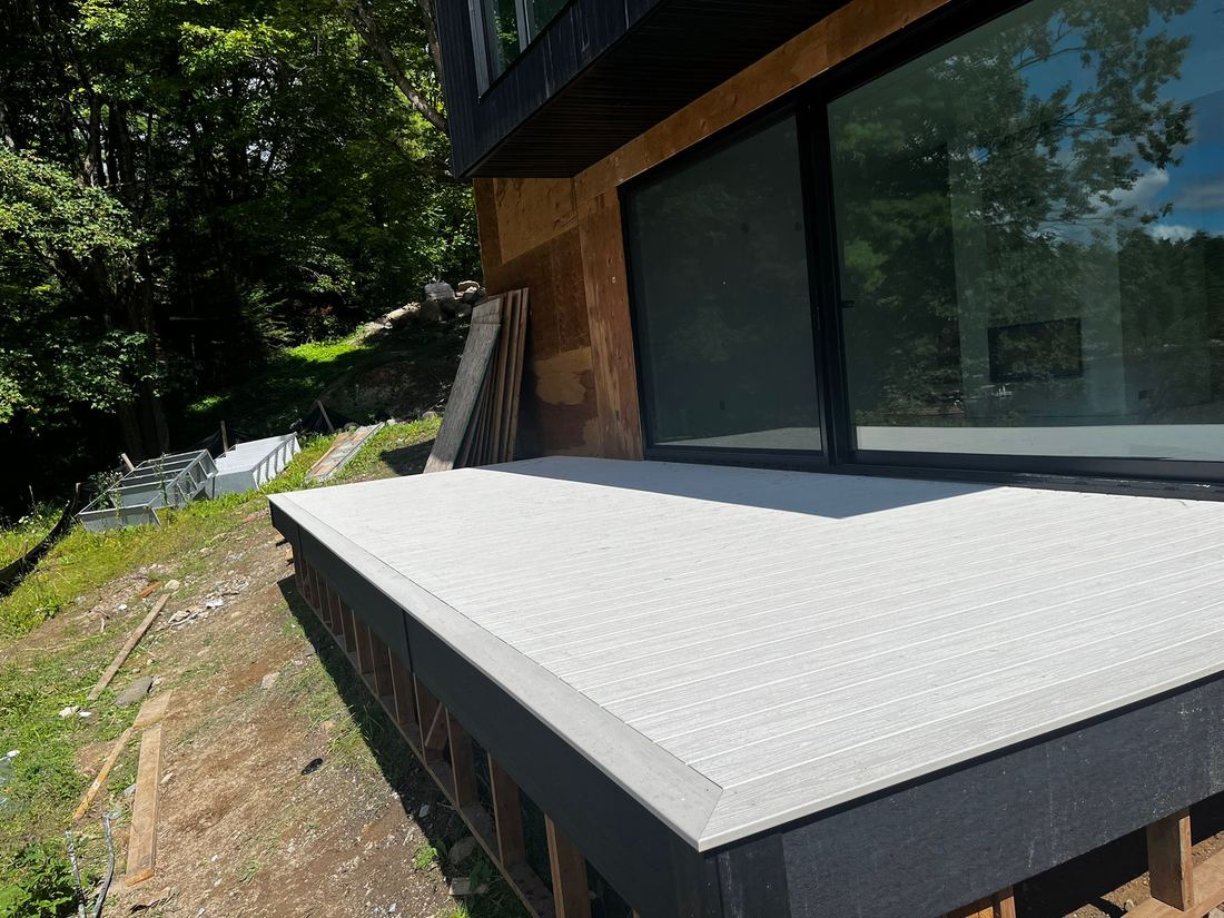 Light grey composite deck with contrast border, work in progress, beside large glass doors