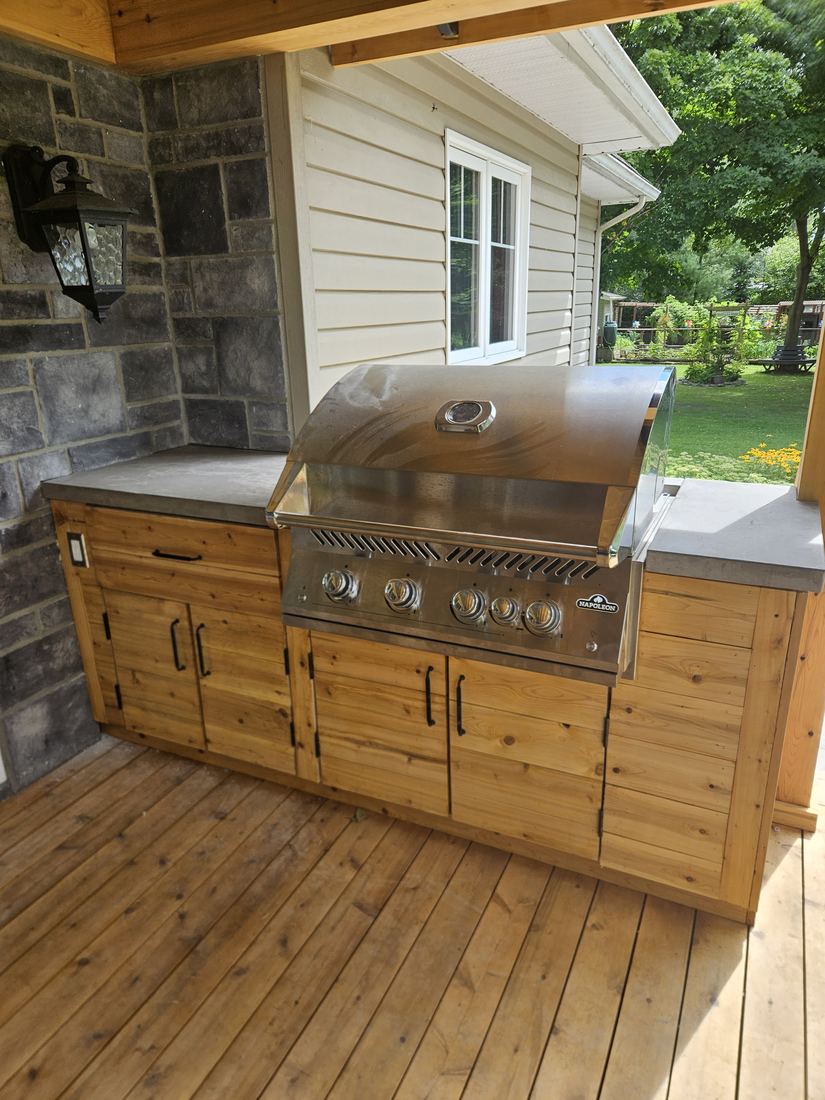 Cedar outdoor kitchen with built-in grill and concrete counter on a covered wood deck