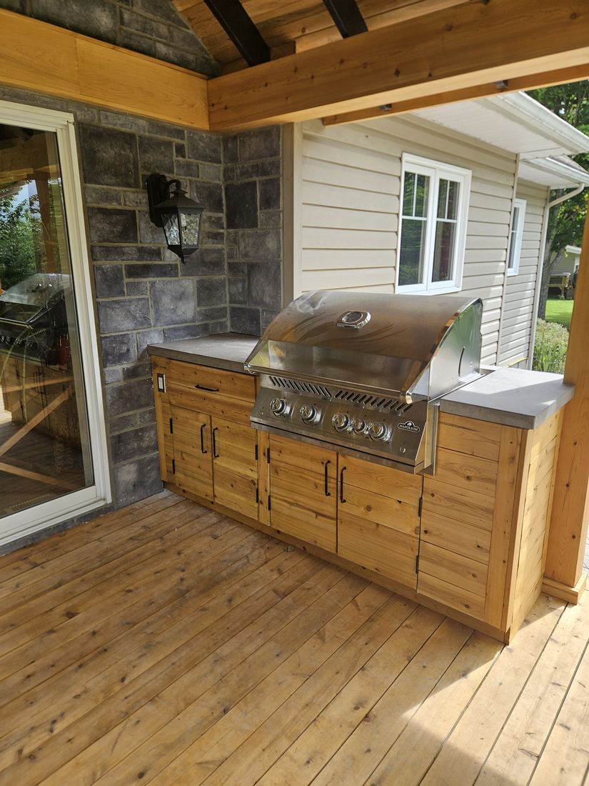 Another view of the cedar outdoor kitchen and wood deck under the roof, stone wall behind