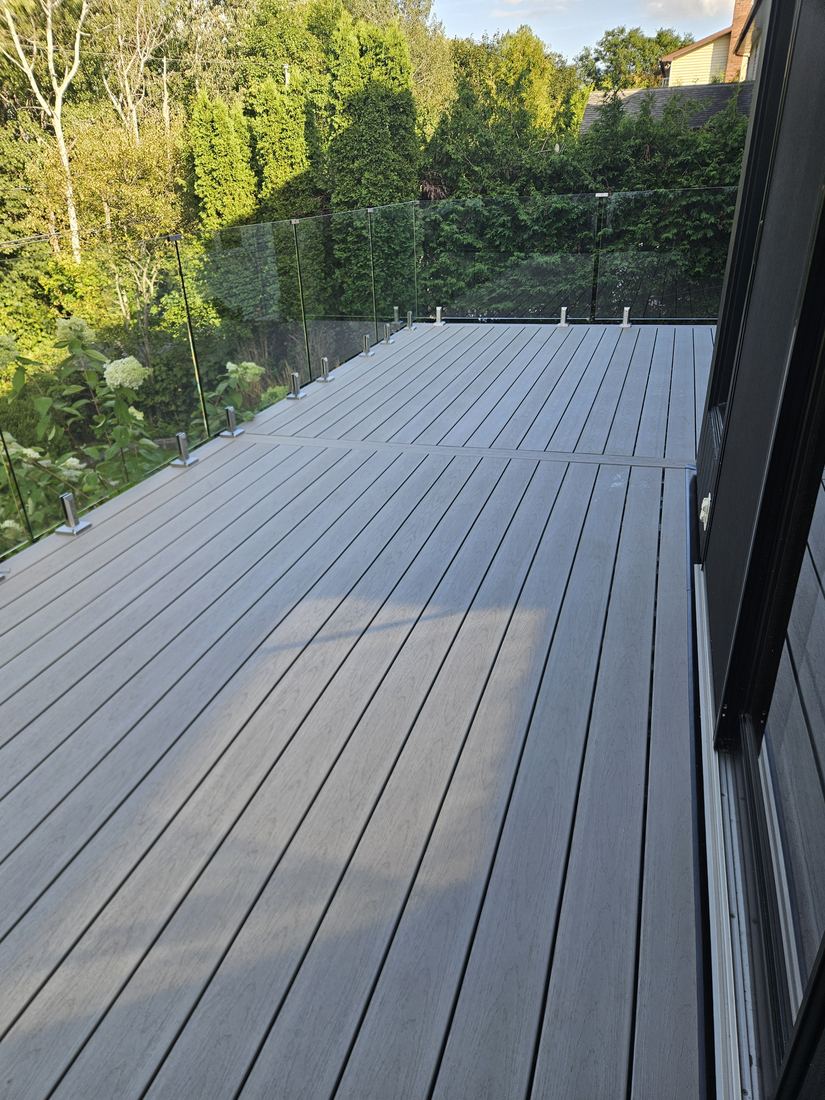 Large grey composite deck with glass railing, looking toward the cedar hedge