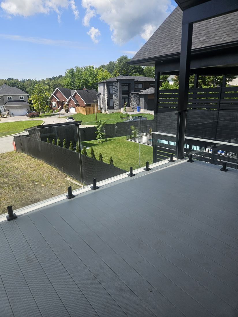 Grey composite deck with glass railing on black posts, overlooking the neighbourhood