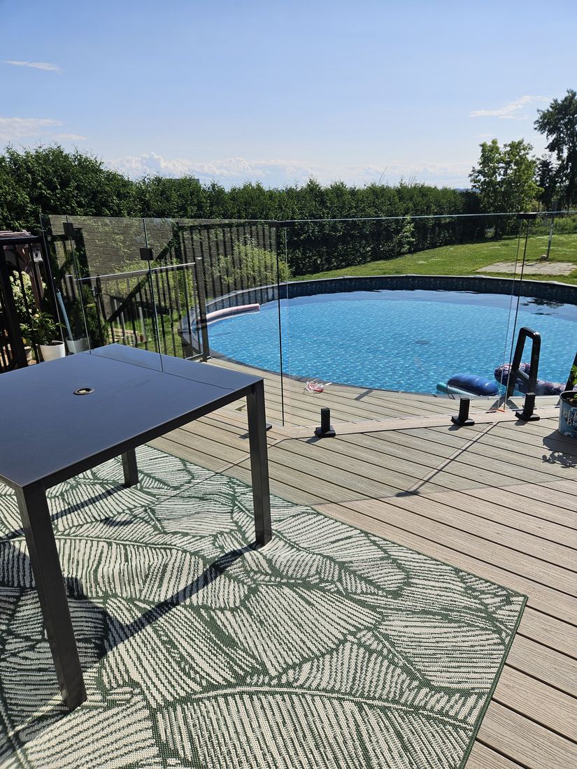 Composite deck around an above-ground pool, enclosed by a glass railing