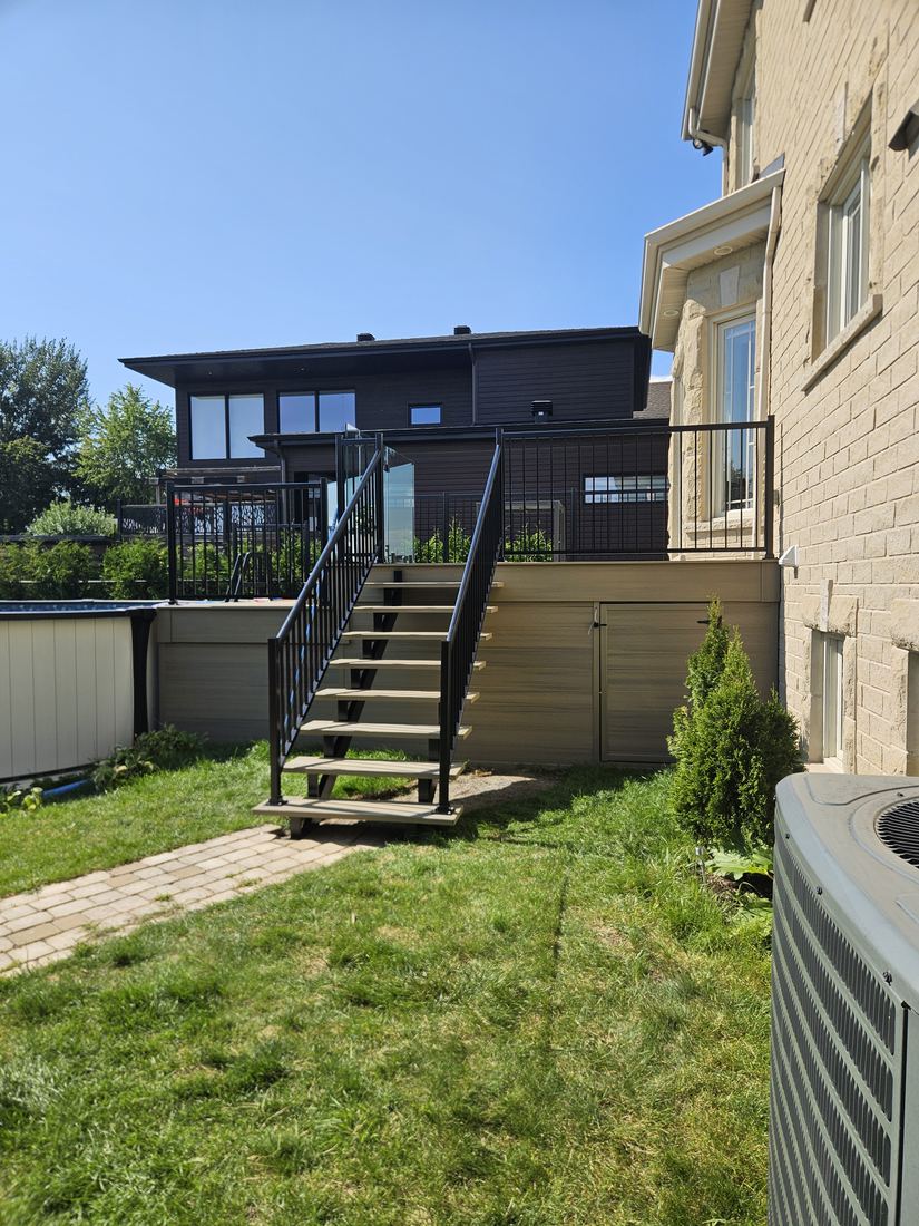 Beige composite stairs with black aluminum railing leading to a raised deck with storage below
