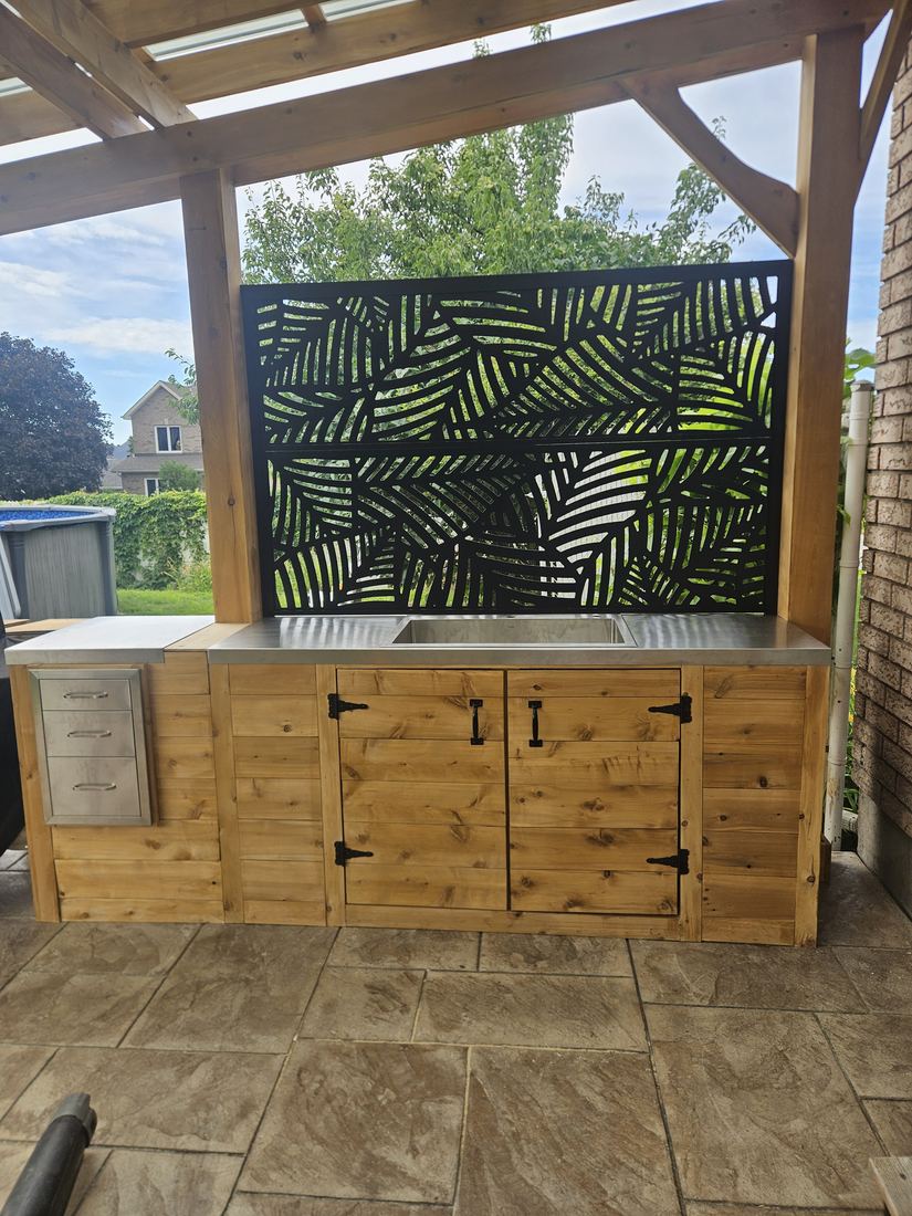 Detail of the cedar outdoor kitchen with sink, steel drawers and black decorative panel under the pergola