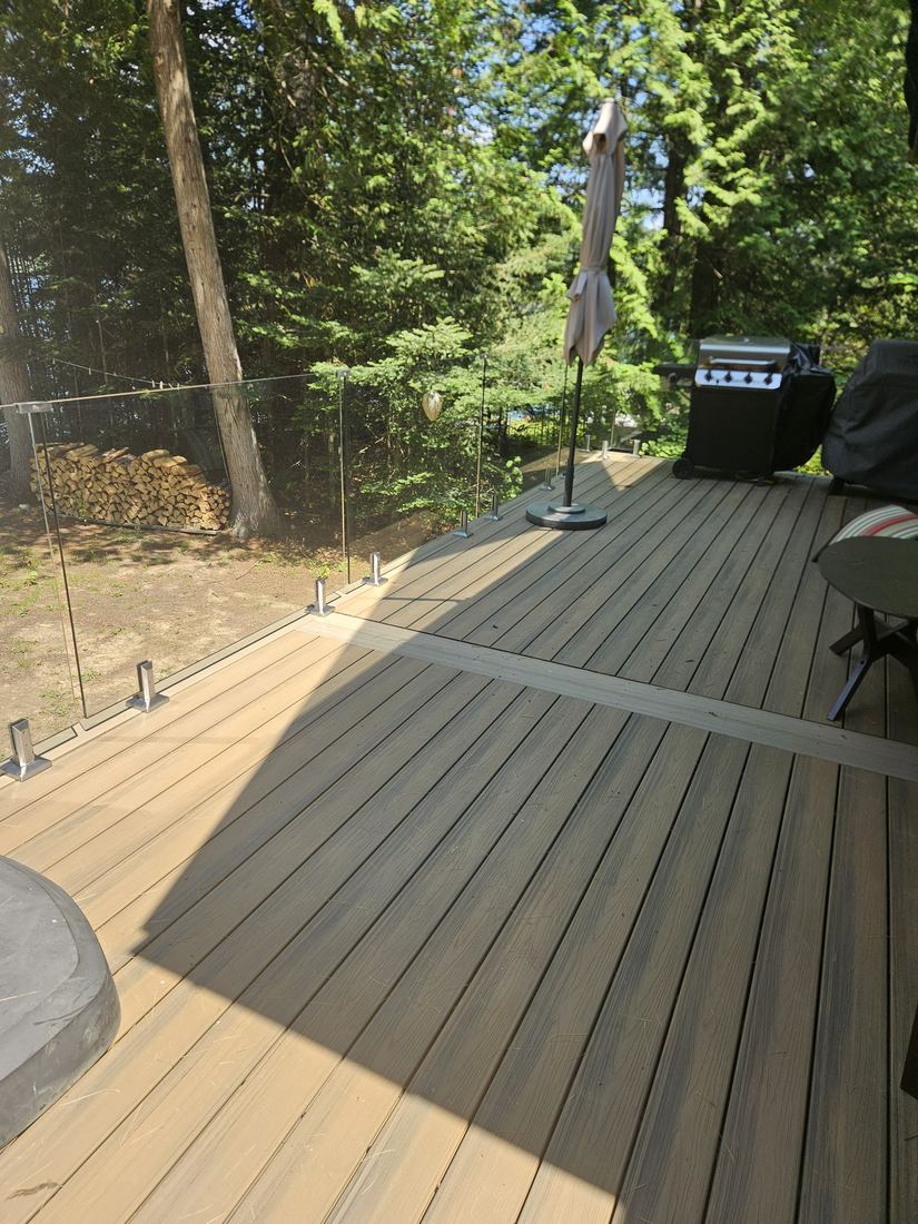 Tan composite deck surface and glass railing, looking out toward the forest