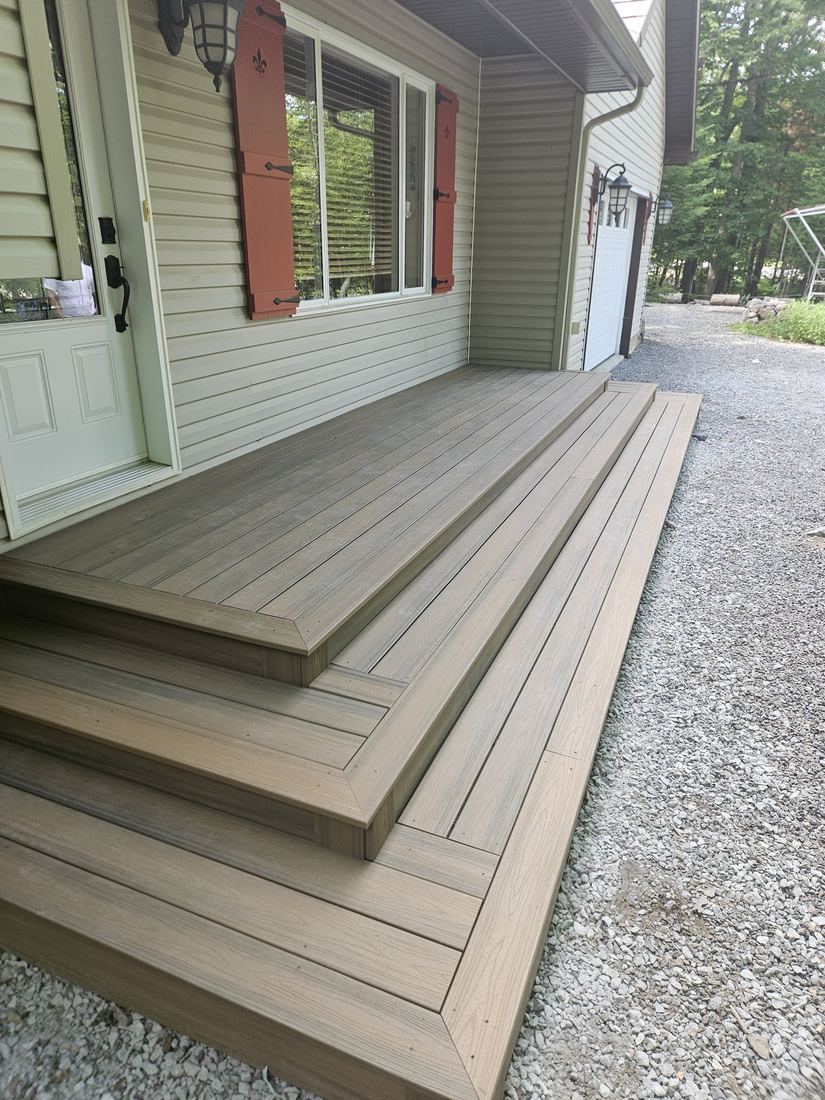 Side view of a multi-step brown composite front porch beside the garage and gravel driveway