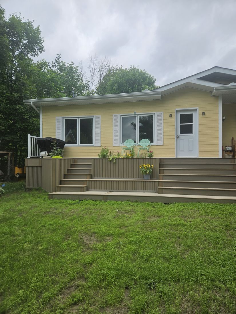 Raised composite deck with wide steps and built-in planters in front of a yellow house
