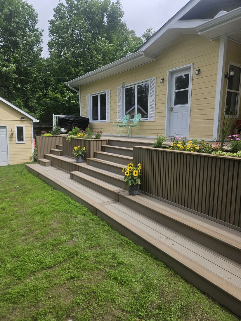 Two-tone composite staircase up to the deck, with a planter wall and pots of sunflowers