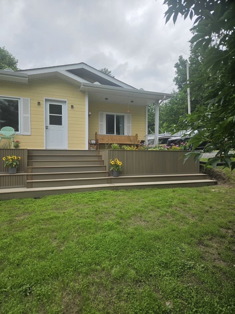 Front view of the composite deck with central stairs and flower planters before a yellow house