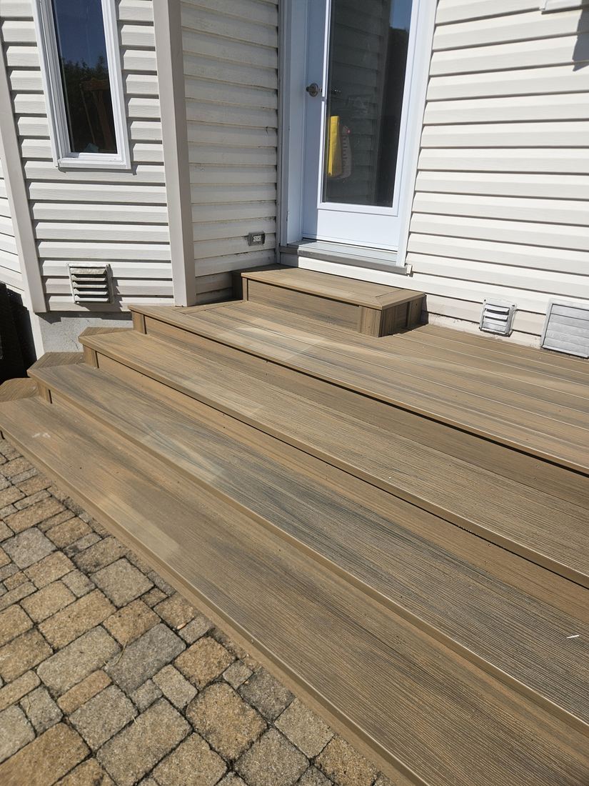 Brown composite steps leading to a door, set on an interlocking paver patio