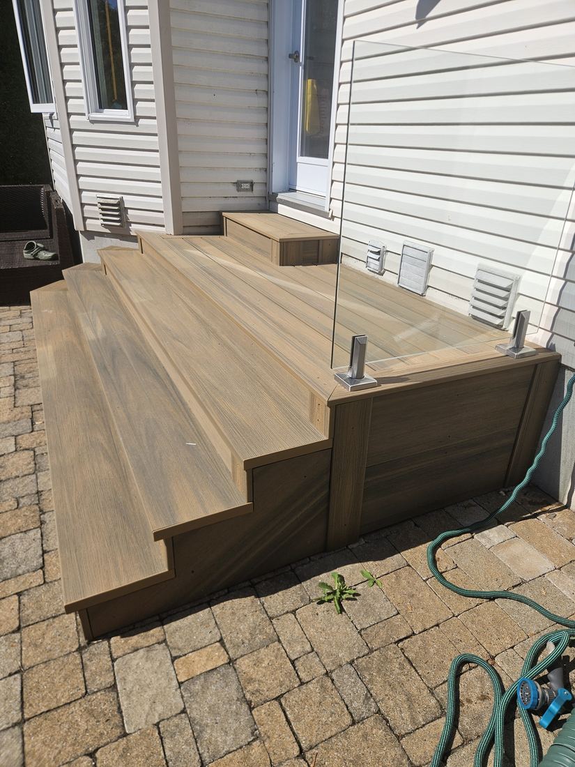 Composite staircase with glass railing and stainless steel posts on an interlocking paver patio