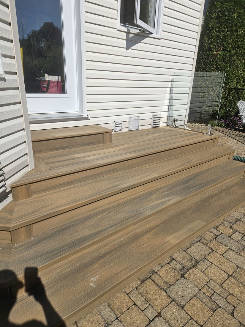 Wide composite steps along the house wall, with a glass panel and pavers alongside