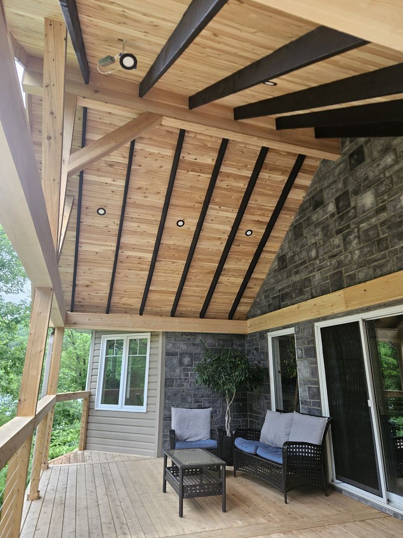 Covered wood deck with cedar ceiling, recessed lights and a seating area before a stone wall