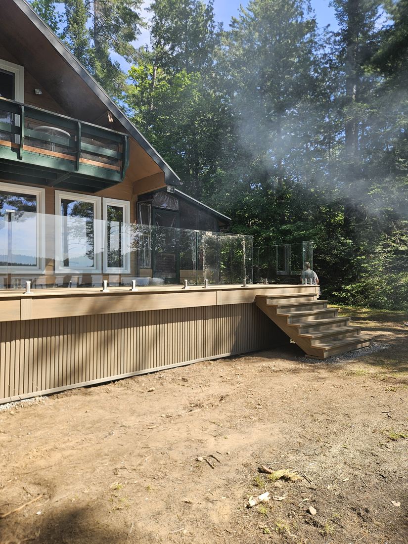 Large composite deck with glass railing, stairs and vertical-slat skirting, in front of a chalet