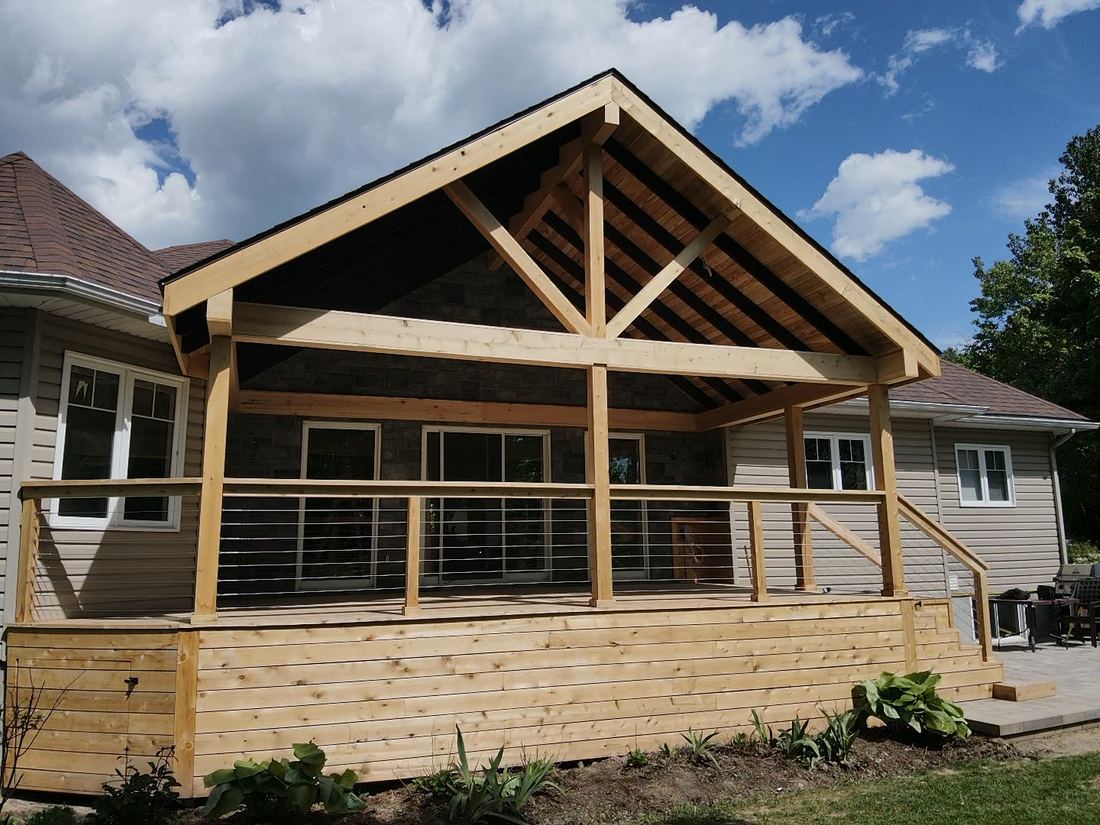 Front view of a covered cedar deck with timber trusses, cable railing and side stairs