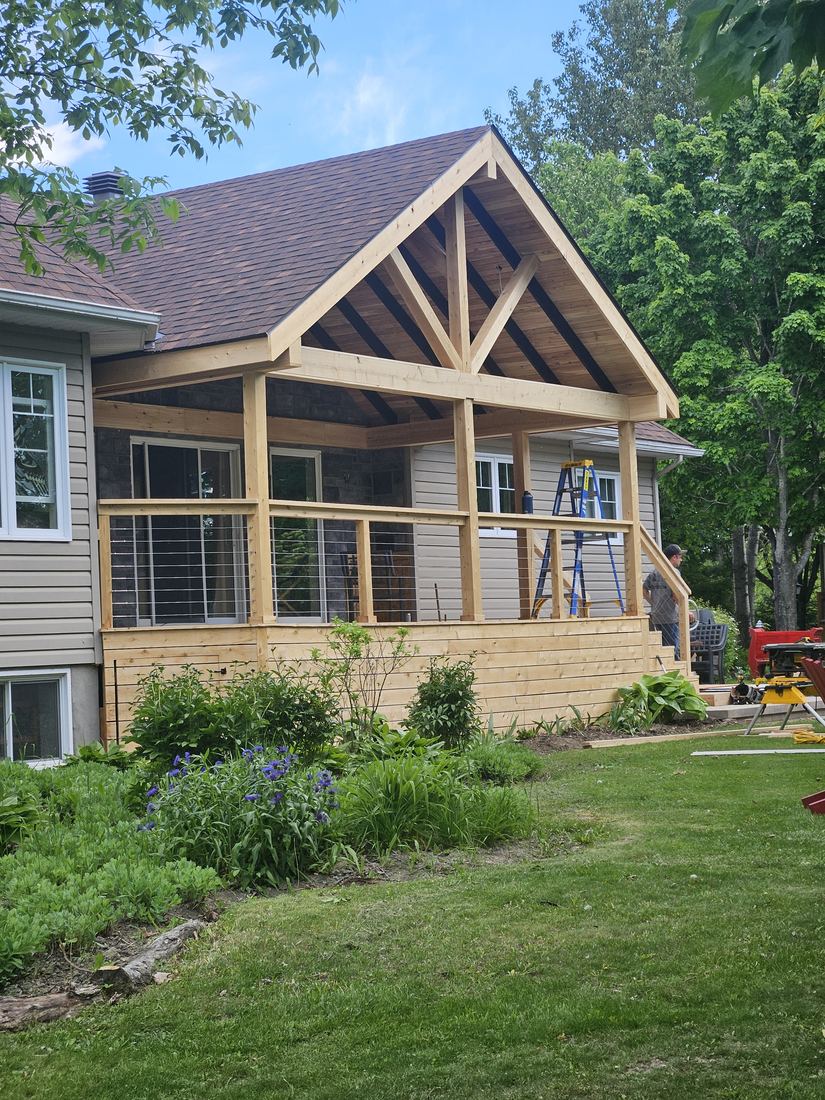Covered cedar deck with gable roof and cable railing, still under construction with ladder and tools