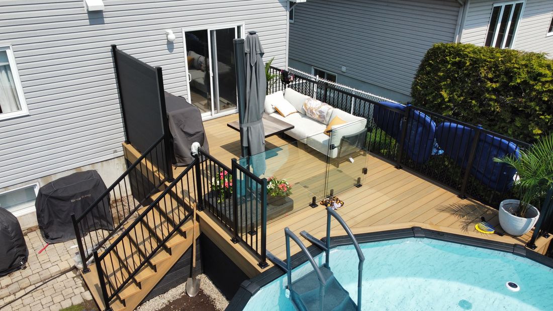 Aerial view of a composite deck with pool, black railing, glass panel and side stairs