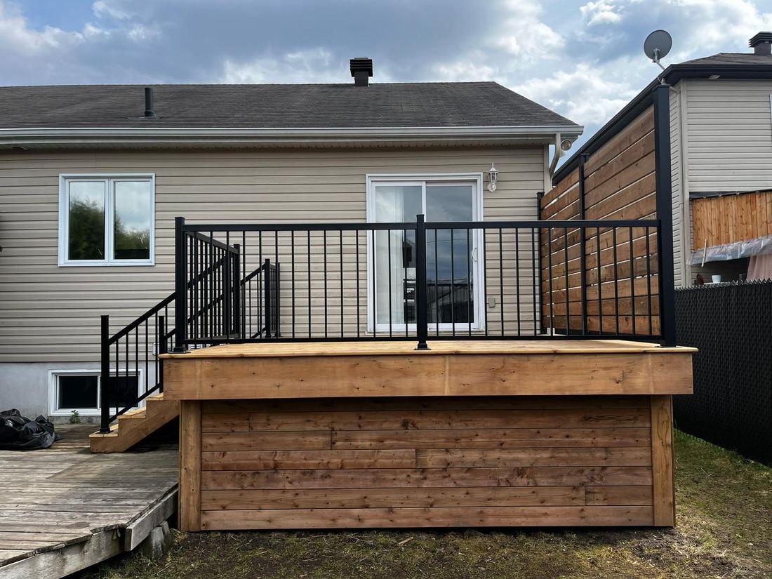 Raised pressure-treated wood deck with black aluminum railing, stairs and slatted privacy screen