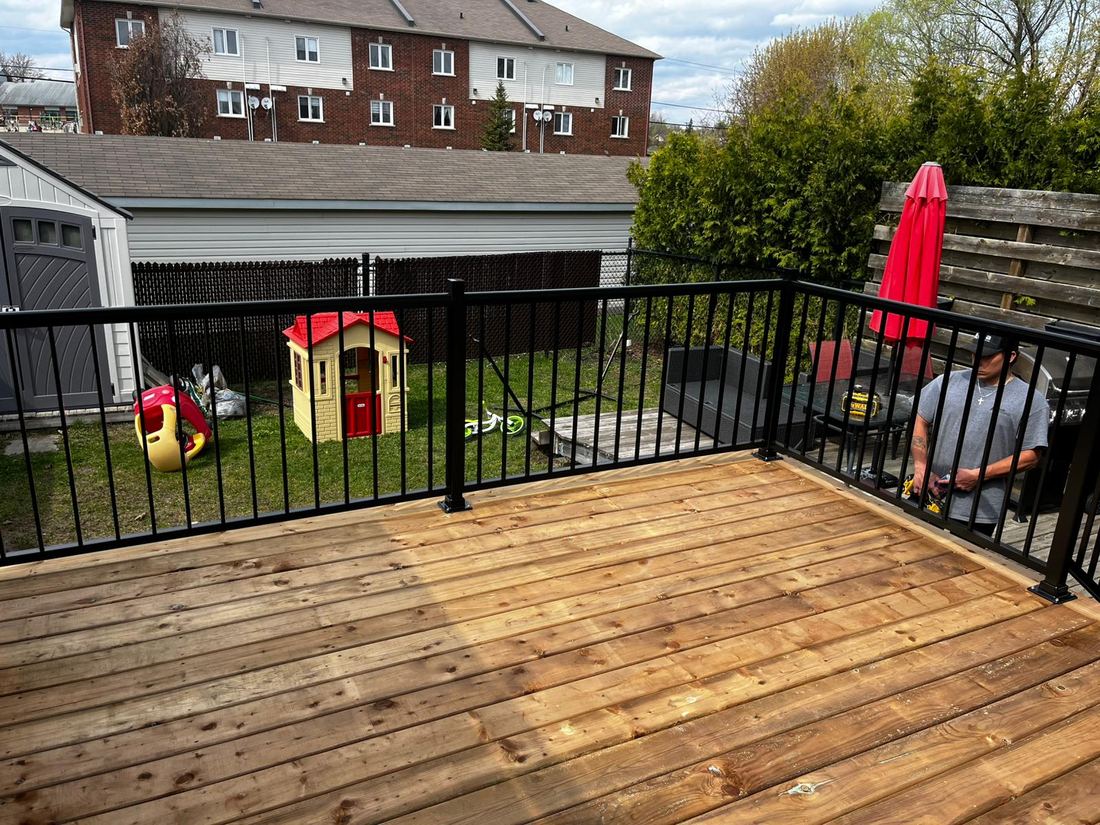 New pressure-treated wood deck with black aluminum railing overlooking the backyard