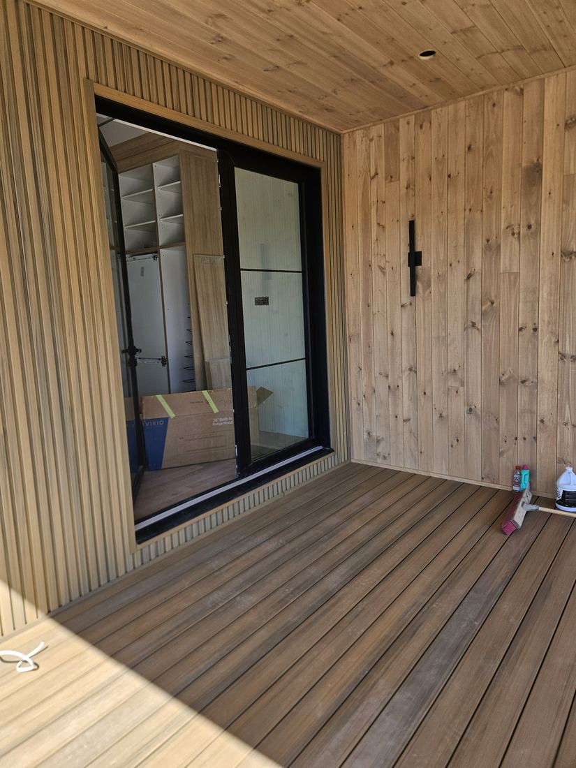 Covered composite deck with wood walls and ceiling by a large glass door, work in progress