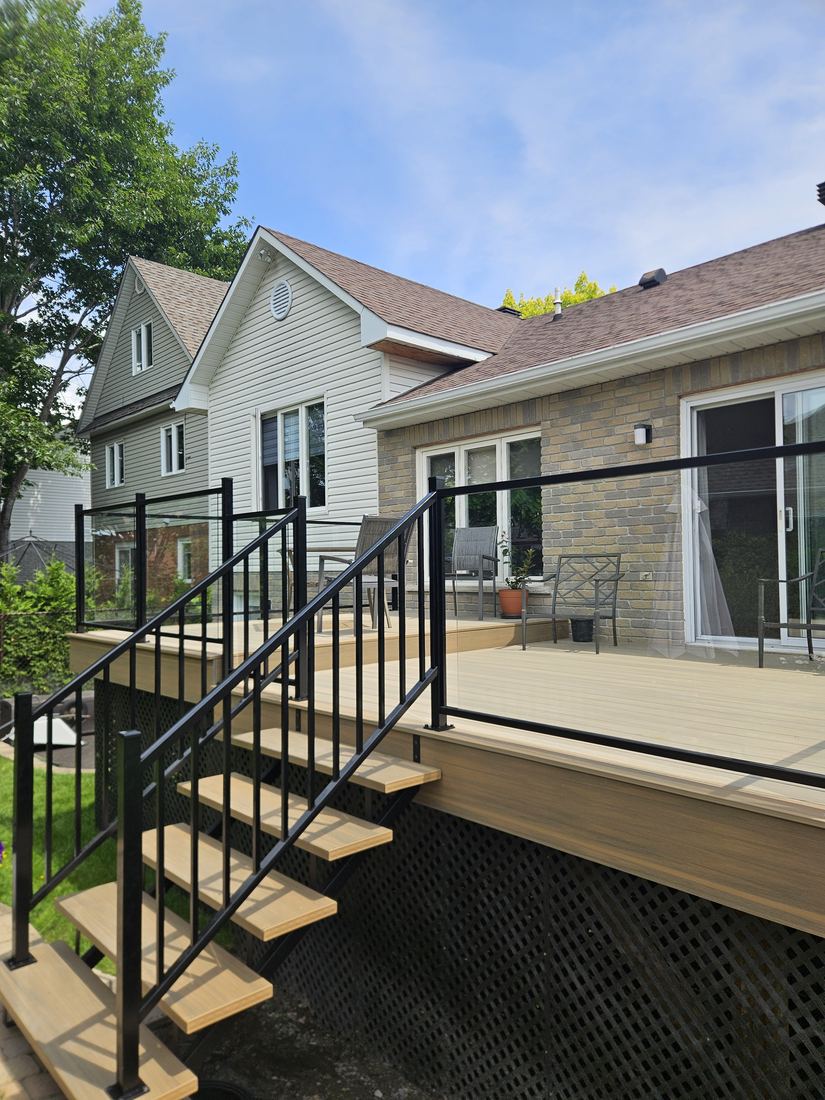 Beige composite deck with glass railing and open-riser stairs with black railing