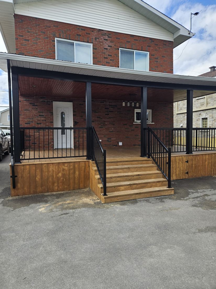 Covered pressure-treated wood porch with black columns, aluminum railing and entry stairs
