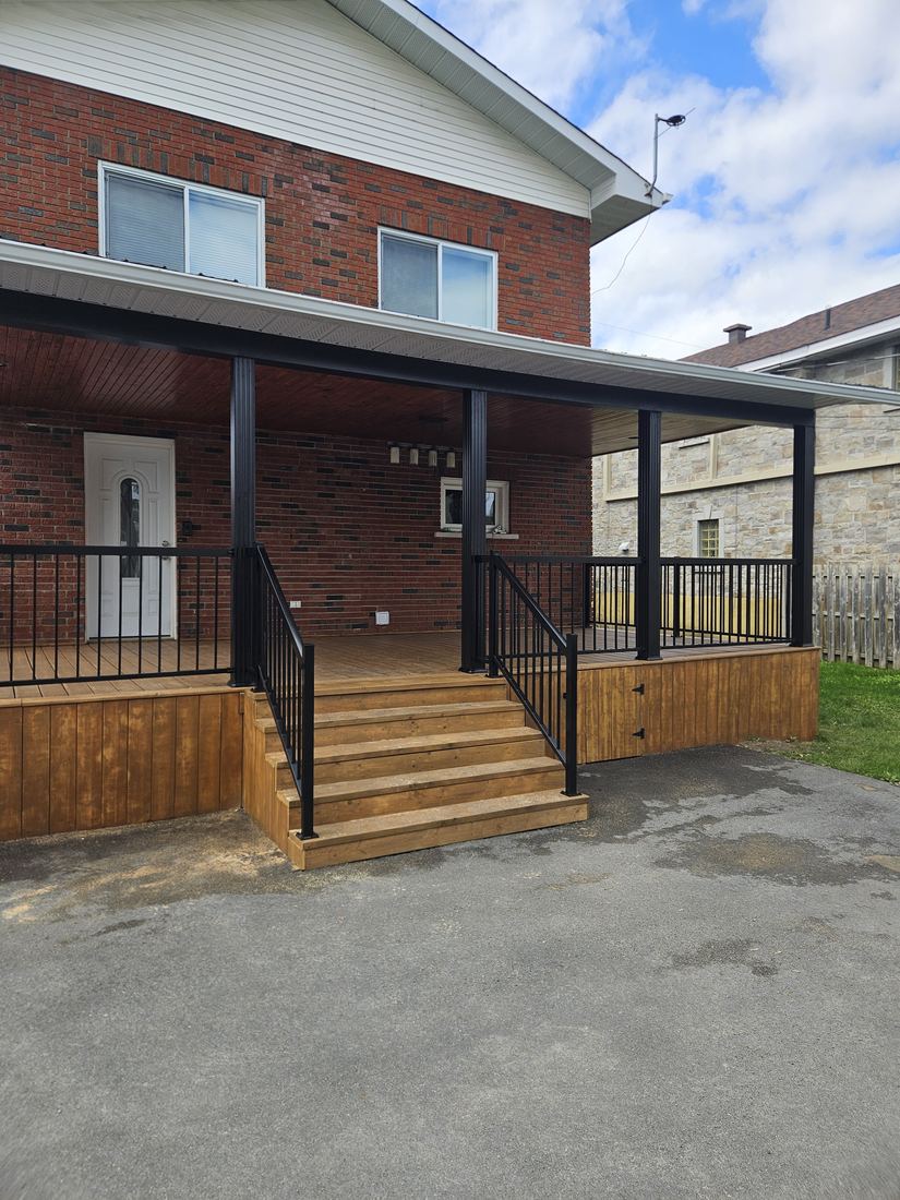 Porch with pressure-treated wood stairs, vertical wood skirting and black railing on a brick house