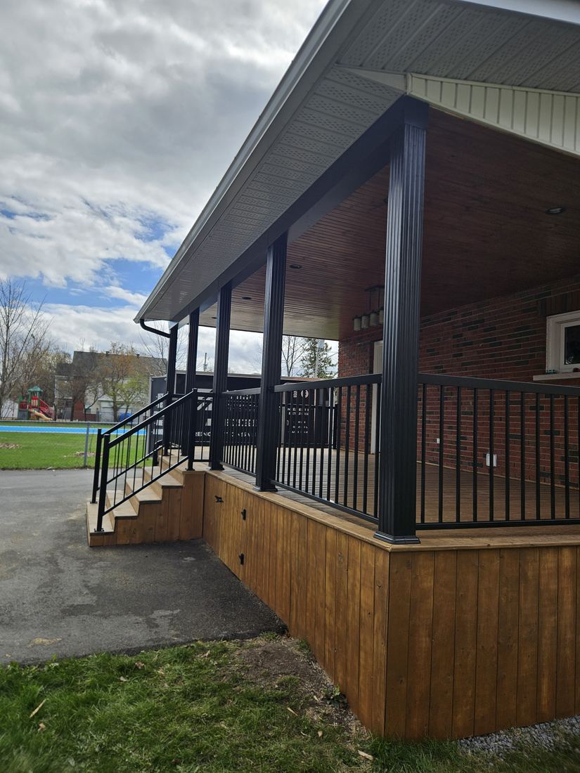 Side view of a covered porch with black columns, aluminum railing and vertical wood skirting