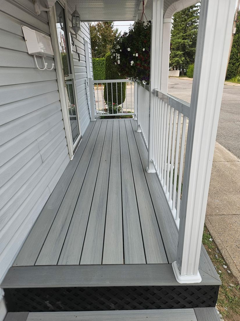 Narrow grey composite porch with white railing, white columns and black lattice skirting
