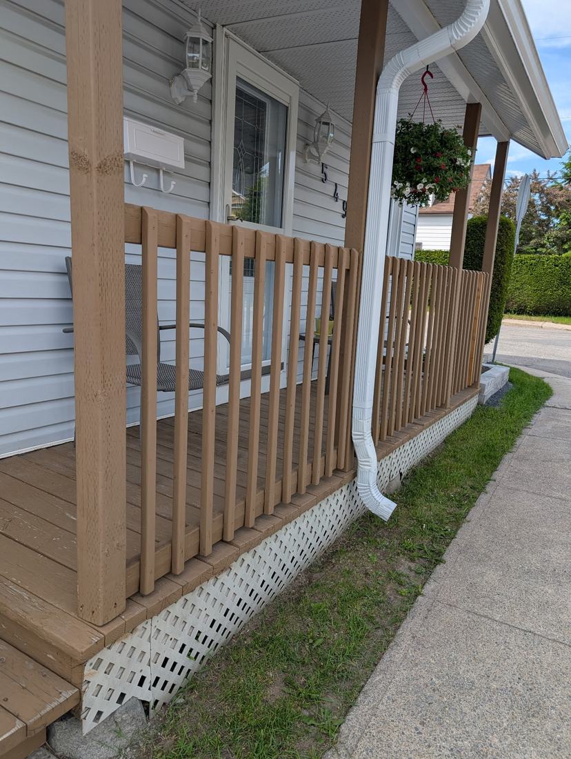 Brown wood porch with vertical-picket railing and white lattice skirting, side view