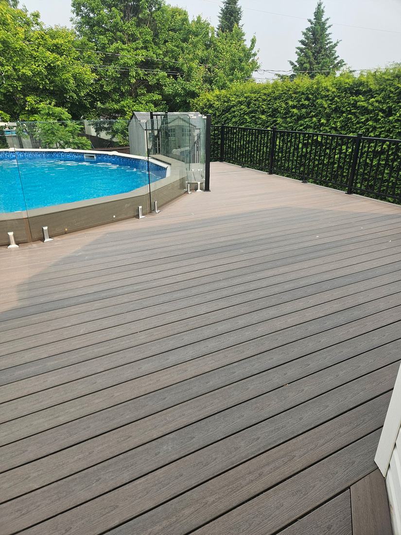 Large brown-grey composite deck around an above-ground pool, with glass and black aluminum railings