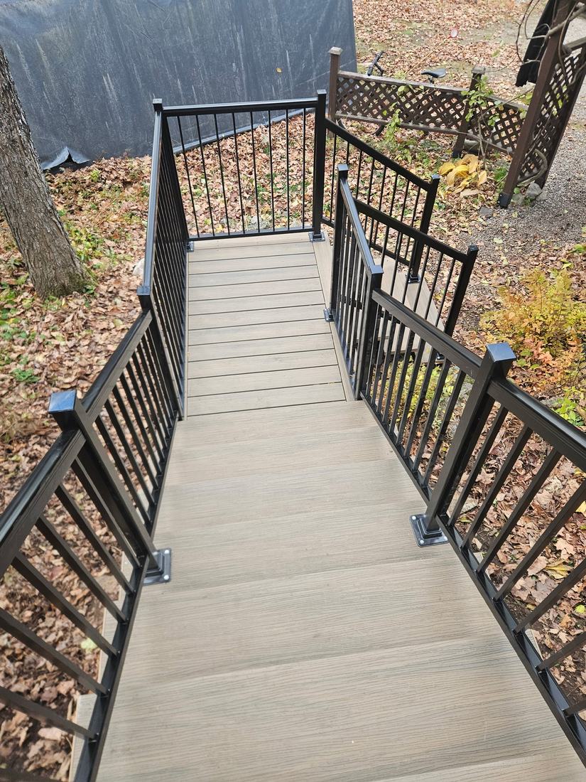 Beige composite stairs and landing with black aluminum railings, seen from above on a sloped lot