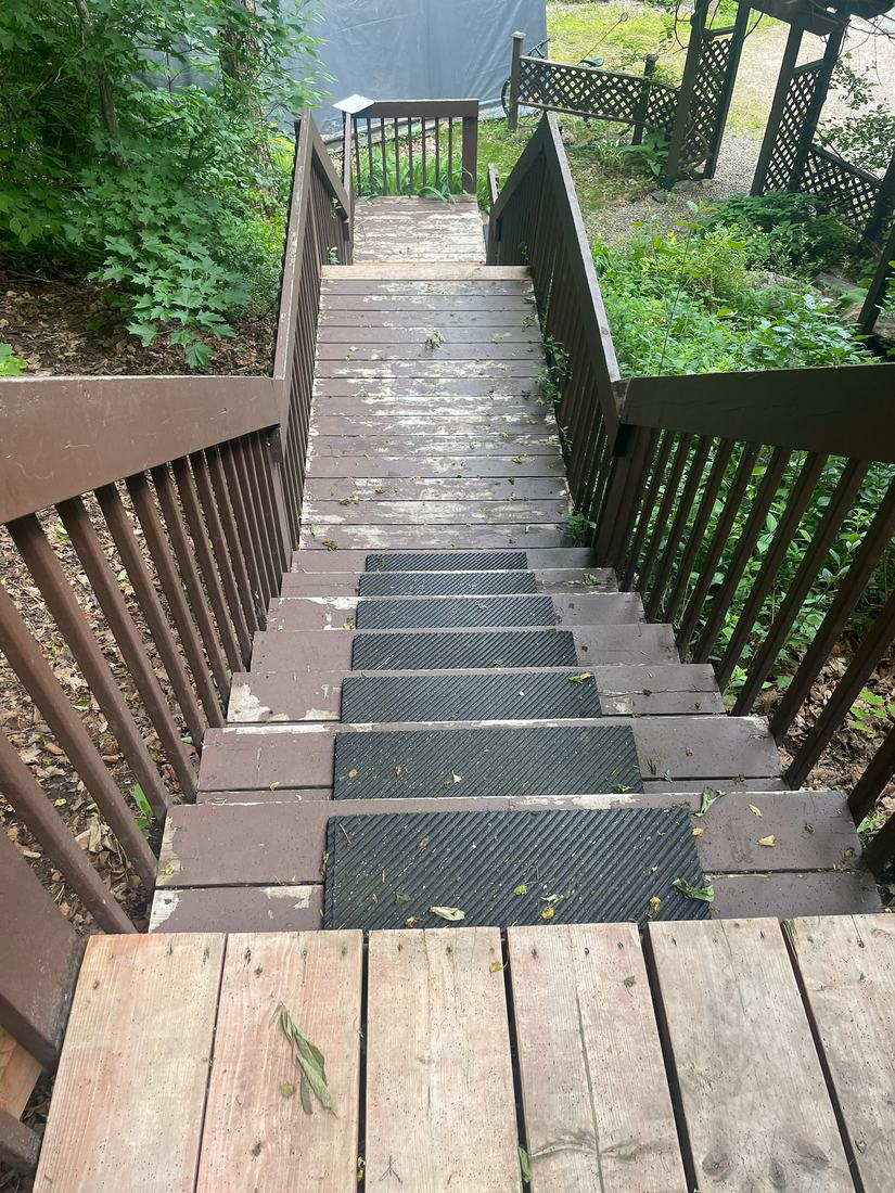 Old brown-stained wooden exterior staircase with worn steps and rubber treads, before renovation