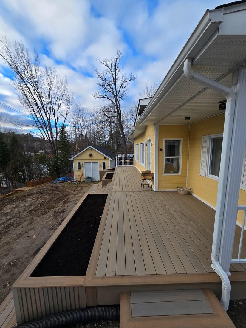 Beige composite deck along a yellow house, with a large built-in raised planter and steps