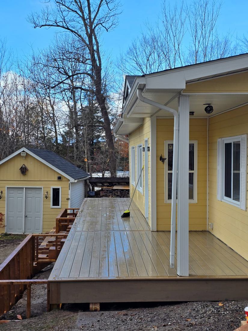 Composite deck under the eave of a yellow house, work in progress, railings not yet installed