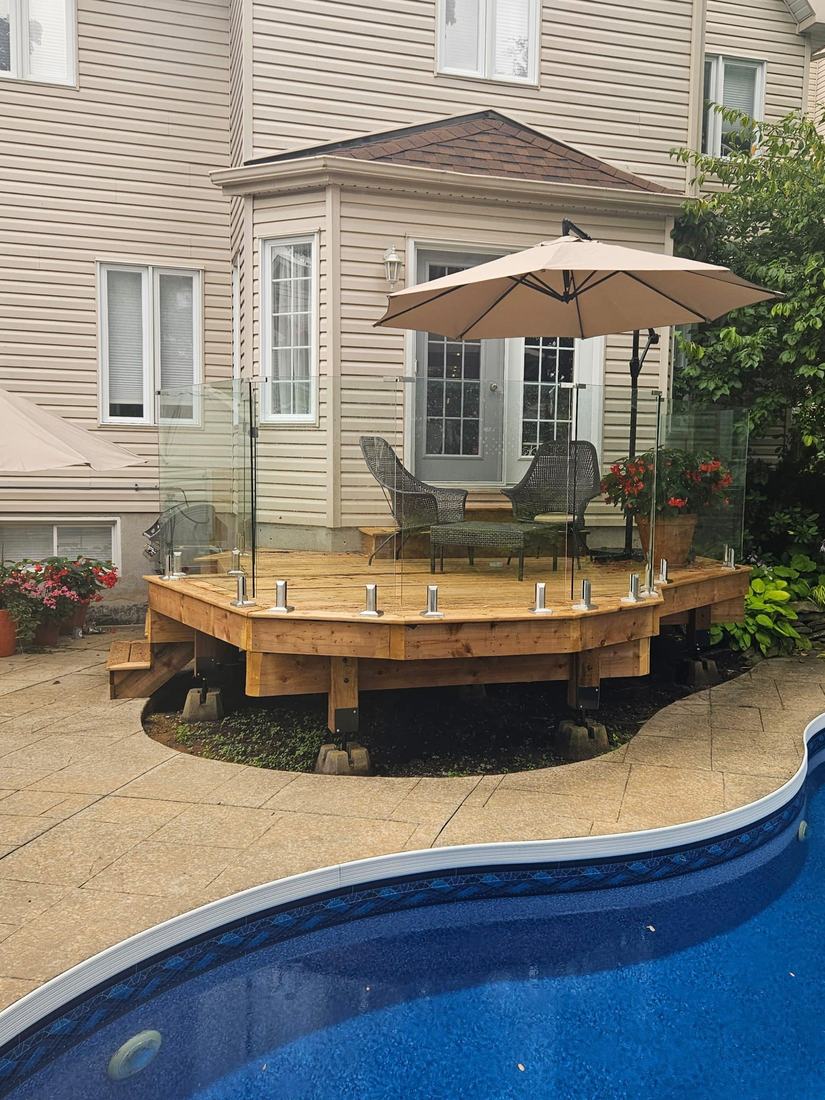 Angled pressure-treated wood deck with glass railing beside an in-ground pool