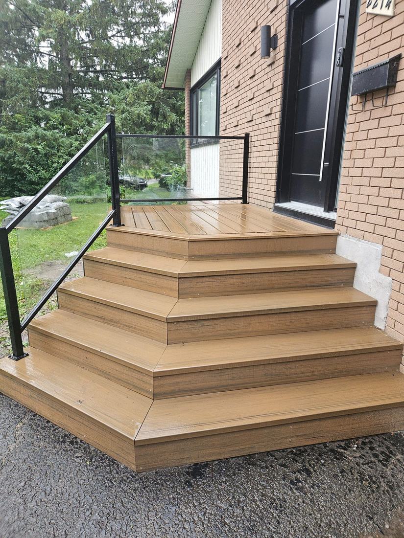 Brown composite entry porch with corner steps and a glass and black aluminum railing