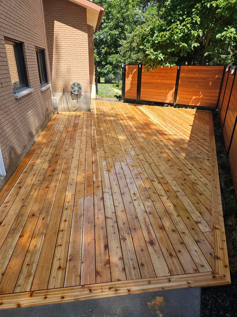 Cedar deck along a brick house, with a framed border and a slatted privacy fence