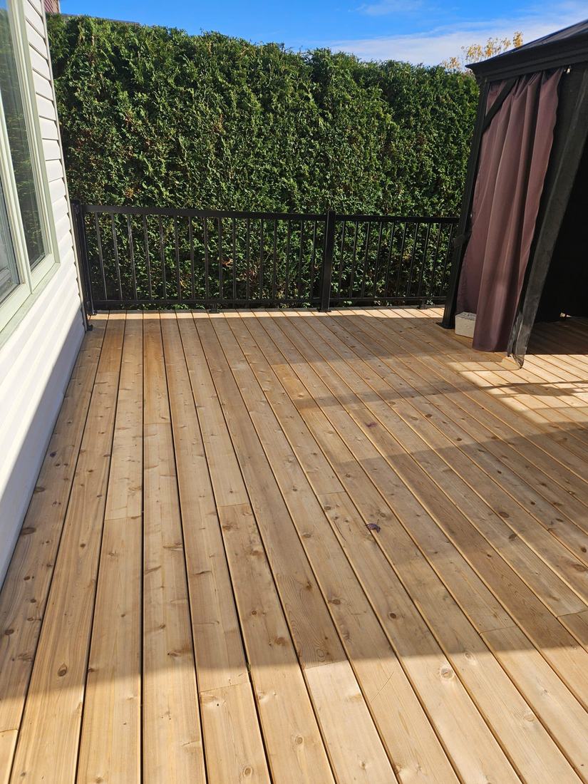 Newly built pressure-treated wood deck with black aluminum railing, next to a curtained gazebo