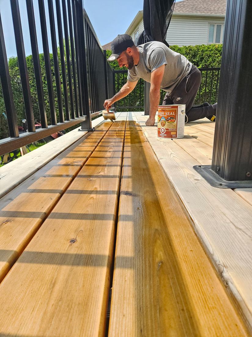 Sealant being brushed onto a new pressure-treated wood deck with a black aluminum railing