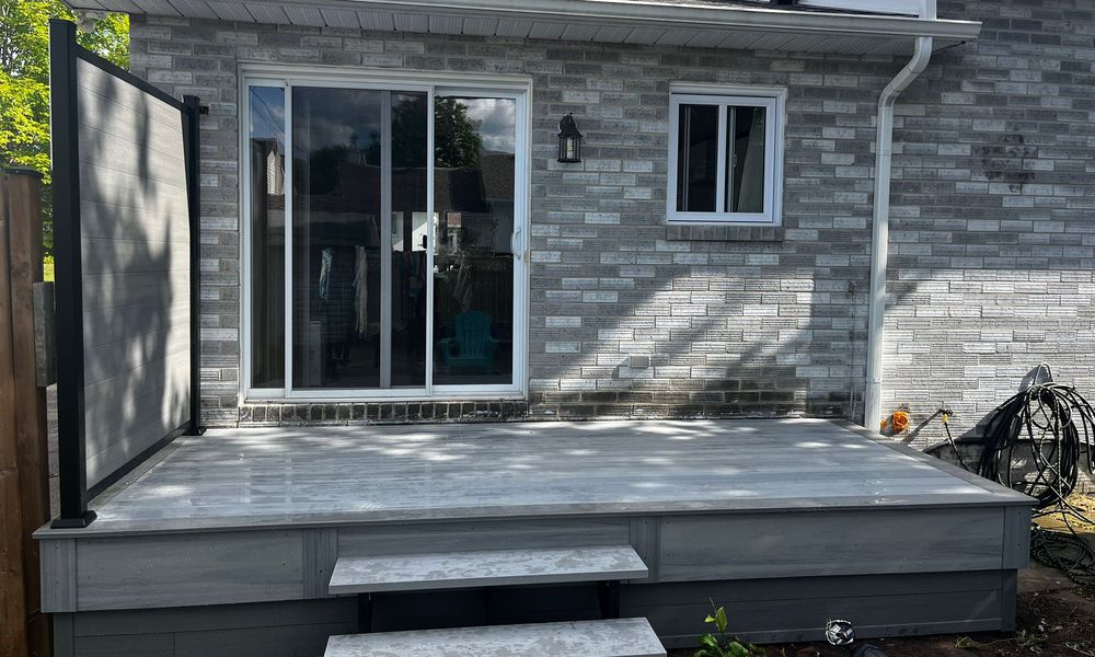 Grey composite deck with a black privacy panel in front of a brick house